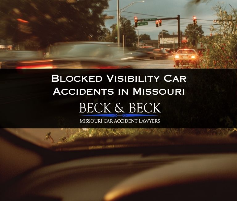 car at an intersection in Jefferson City, Missouri with heavy bushes and foliage to the right, blur of cars speeding by in front.